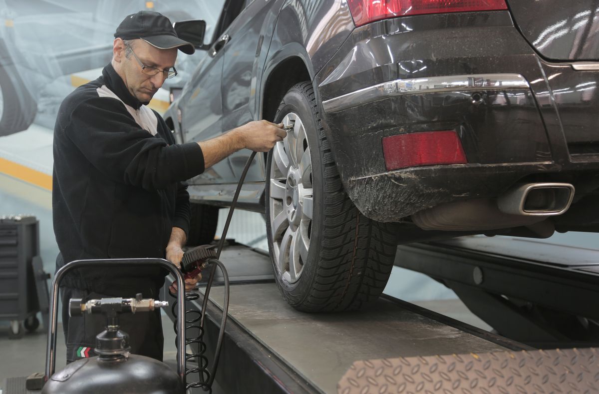 Mechanik kontroluje tlak v pneumatice vozu na zvedáku