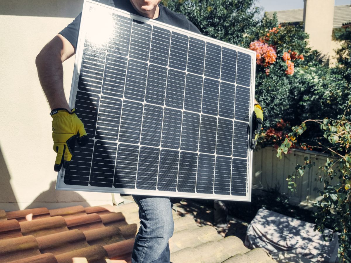 Montážník nese solární panel na střechu