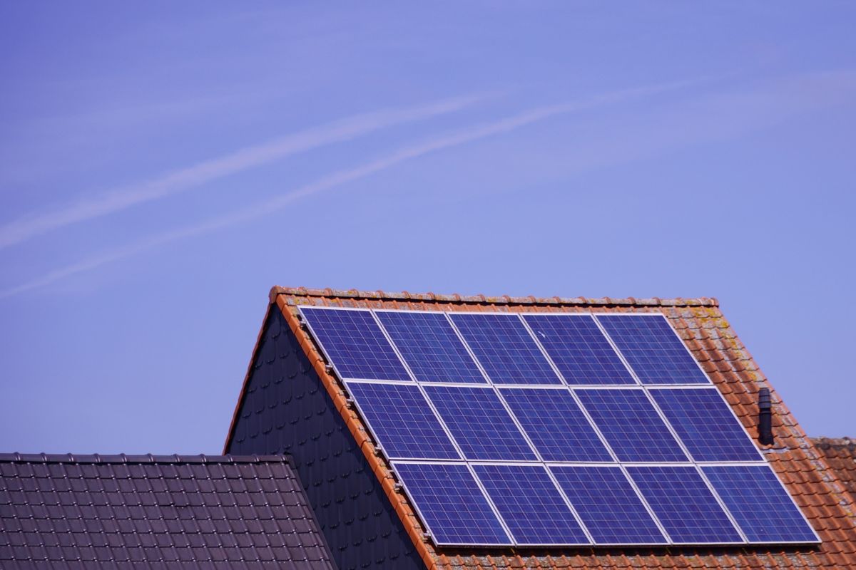 Střecha rodinného domu s fotovoltaickými panely proti modré obloze