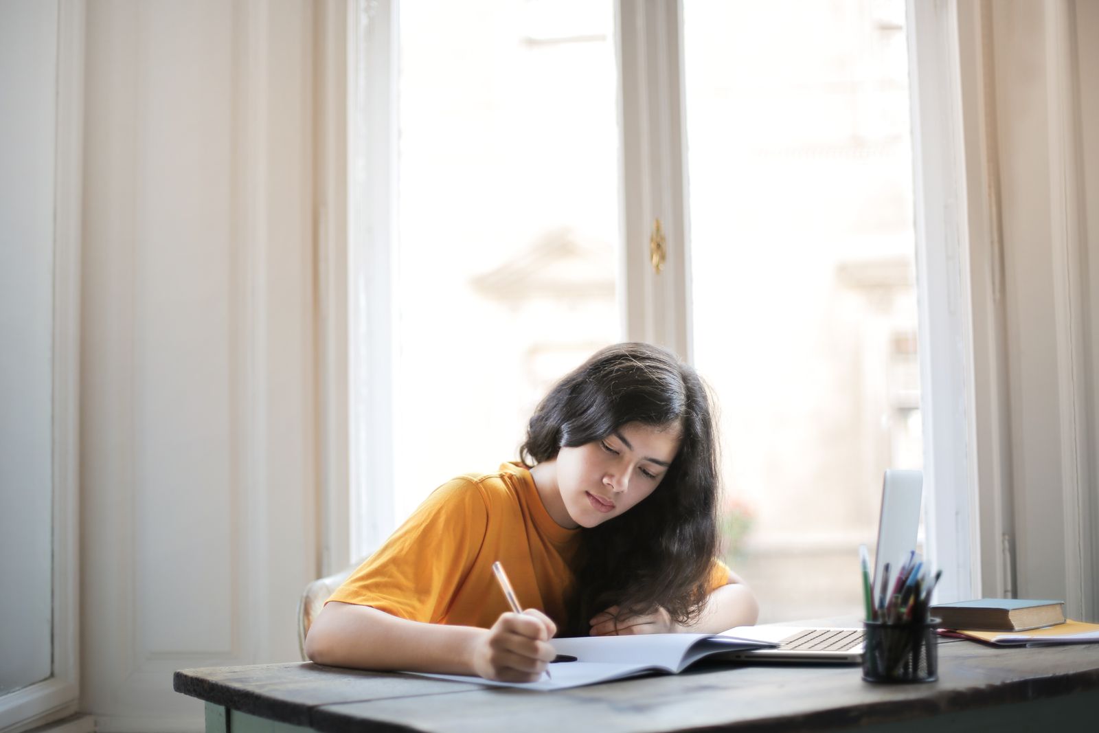 Studentka se učí u stolu s učebnicí a sešitem