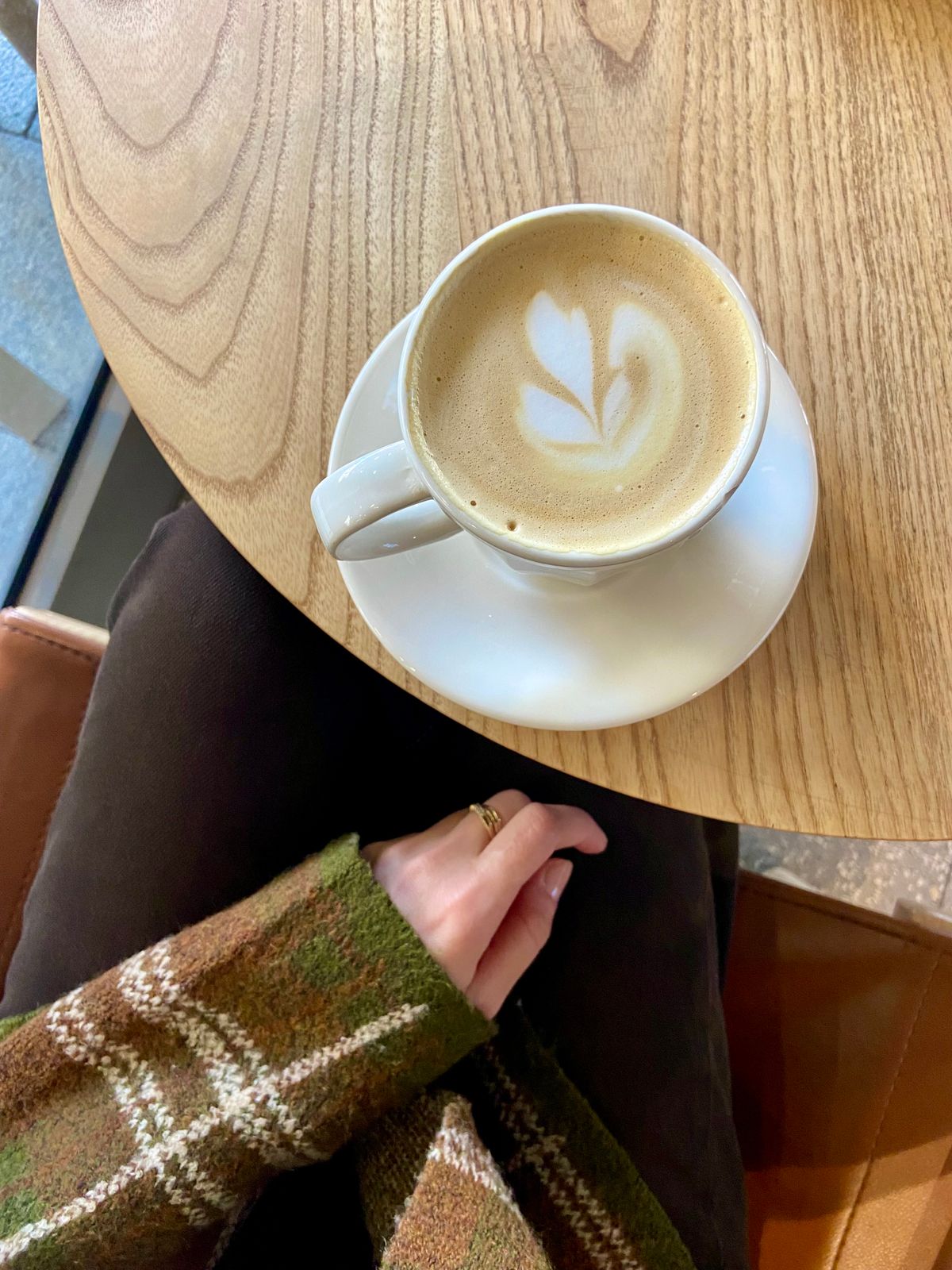 Šálek kávy s latte art na světlém dřevěném stolku