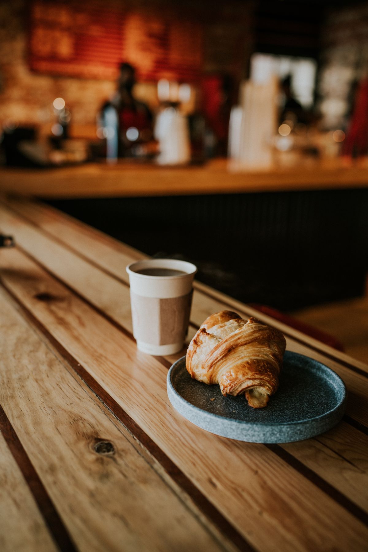 Káva a čerstvý croissant na dřevěném pultu kavárny