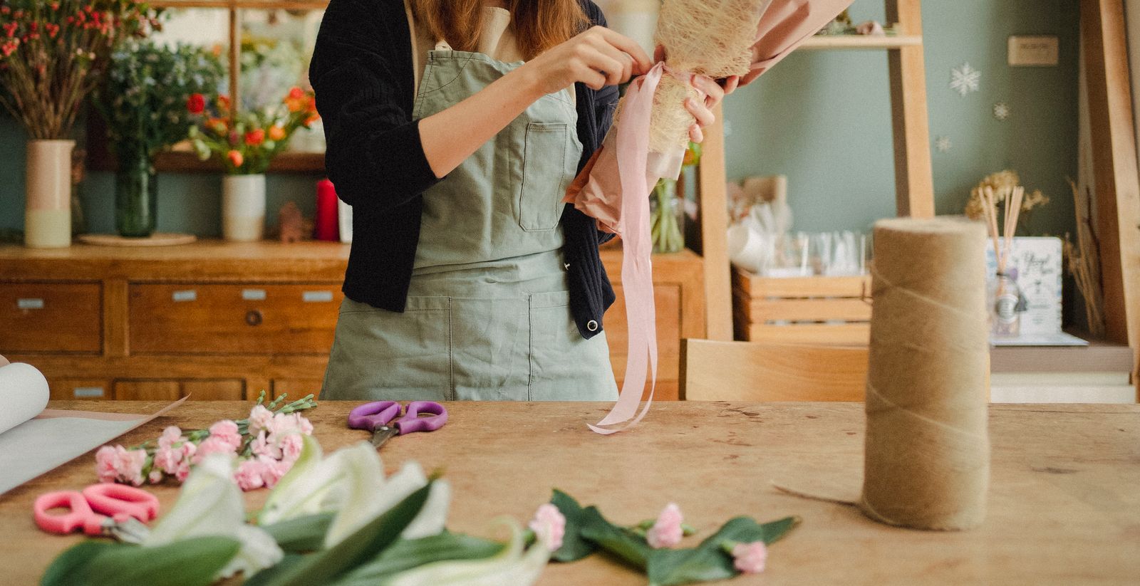 Floristka váže kytici z růžových květin na pracovním stole